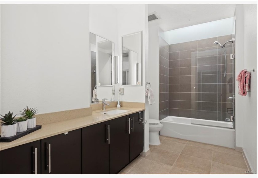 133 The Promenade N #318 — bathroom with dual vanity, quartz counter, and tiled shower